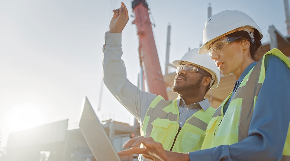 Construction professionals pointing up and using a laptop at a construction site