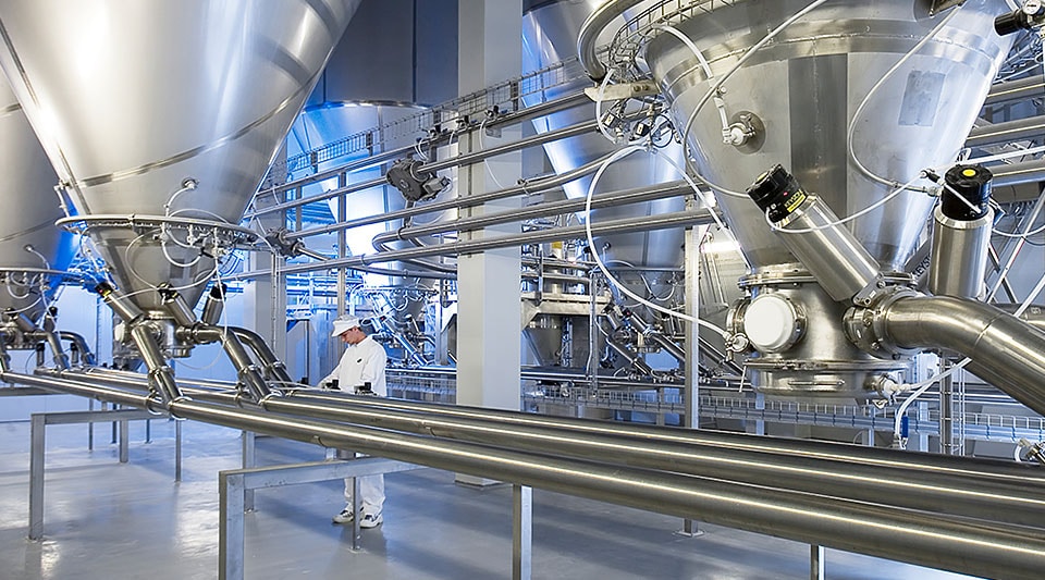 A man working with a large industrial processing system comprised of metal valves and pipes